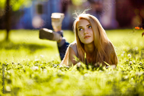 A beautiful girl lies in the park on the grass and dreamily looks around