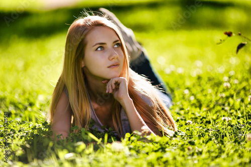 A beautiful girl lies in the park on the grass and dreamily looks around