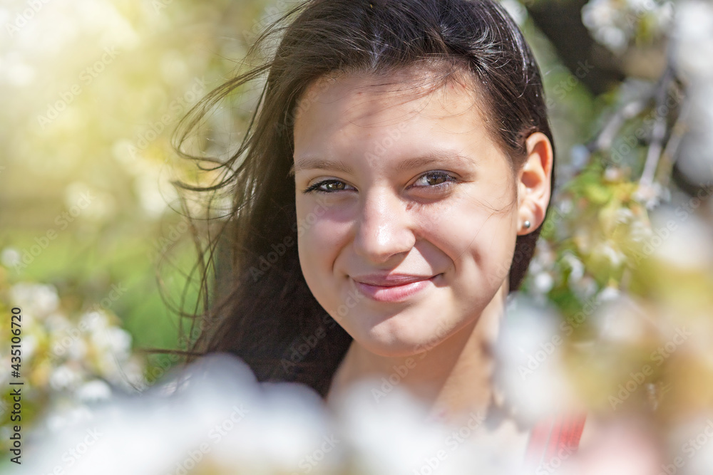 Closeup view of smiling black long hair girl posing in blooming tree. Horizontally. Closeup view of smiling black long hair girl posing in blooming tree. Horizontally.