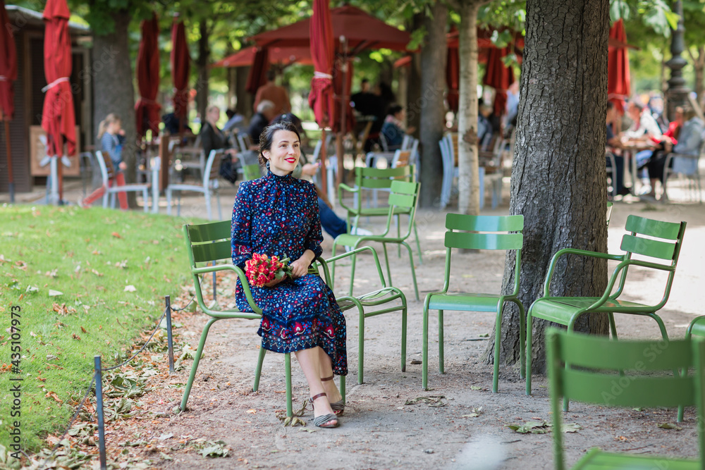 Smiling woman in a dark blue dress sitting in a chair in the park