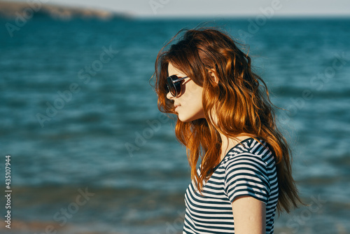 red-haired woman in sunglasses on the beach near the blue sea and mountains in the background