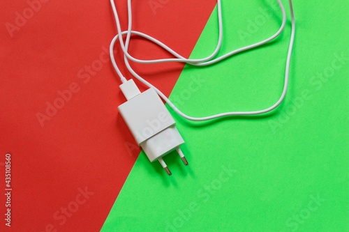 White phone charger isolated on half red half green background. Technological devices. Top view.