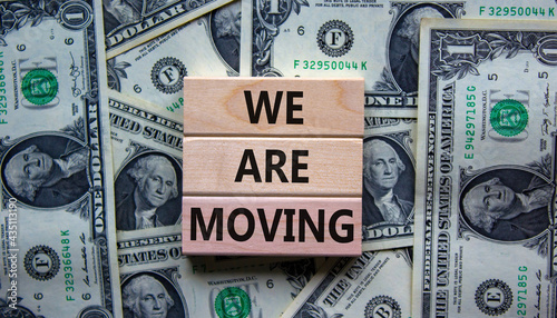 We are moving symbol. Wooden blocks with words 'We are moving'. Beautiful background from dollar bills. Business, we are moving concept, copy space.