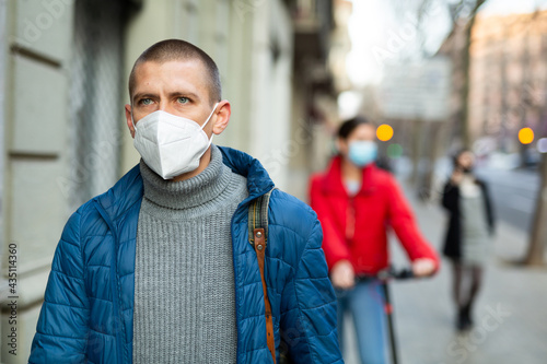 Portrait of young urban man in a protective face mask wearing winter clothes walking street