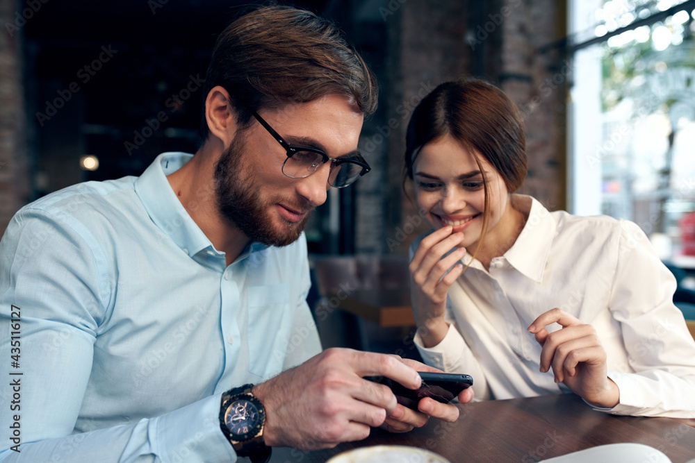 Cheerful man and woman are sitting in a cafe at the table working communication technology