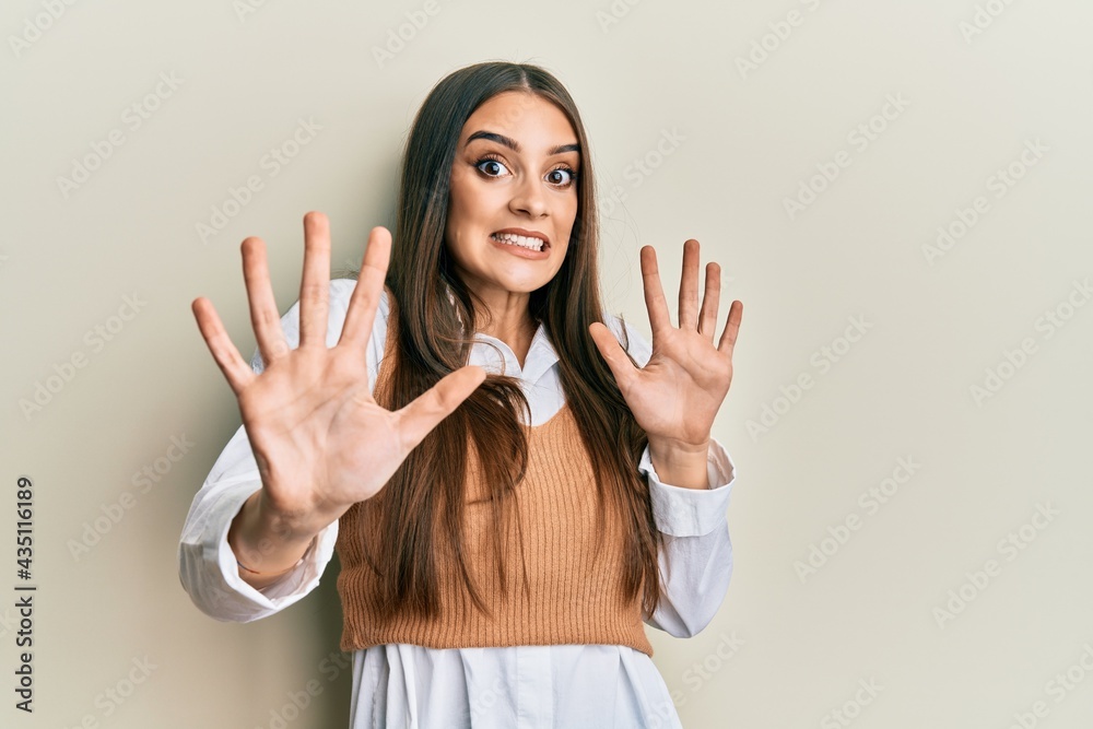 Beautiful brunette young woman wearing casual clothes afraid and terrified with fear expression stop gesture with hands, shouting in shock. panic concept.