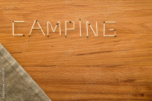 Matches and a piece of canvas on a wooden table. Matches form the word "CAMPING"