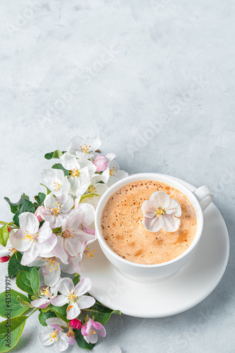 A white cappuccino cup and beautiful flowers on a light gray background.