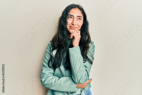 Fotografie Hispanic teenager girl with dental braces wearing green leather jacket thinking