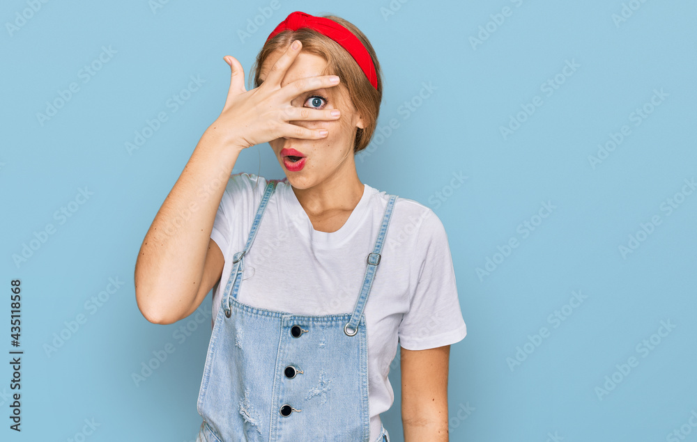 Young caucasian girl wearing casual clothes peeking in shock covering face and eyes with hand, looking through fingers with embarrassed expression.