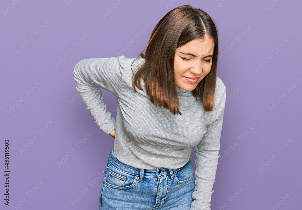 Young beautiful woman wearing casual turtleneck sweater suffering of backache, touching back with hand, muscular pain Young beautiful woman wearing casual turtleneck sweater suffering of backache, touching back with hand, muscular pain