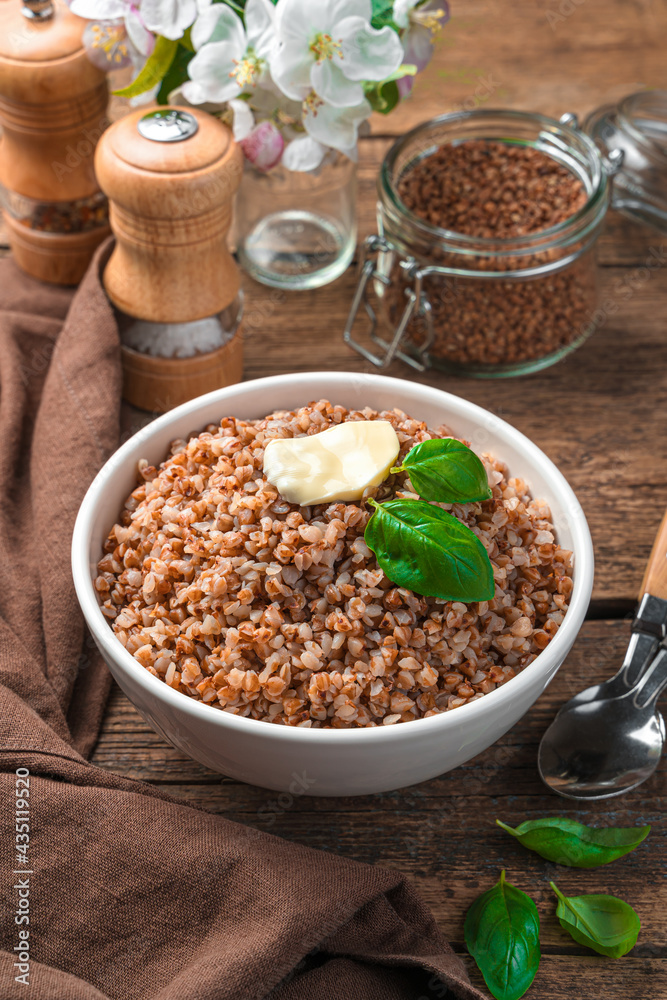 Buckwheat with butter and basil in a white plate on a brown background. Buckwheat with butter and basil in a white plate on a brown background.