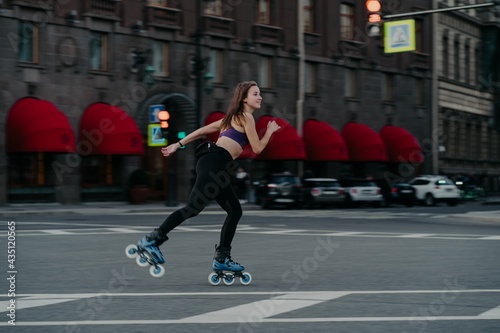 Extreme sport recreation and fitness activity concept. Active woman rides on rollers in urban environment strengthens leg muscles demonstrates high level of stability balances on small wheels