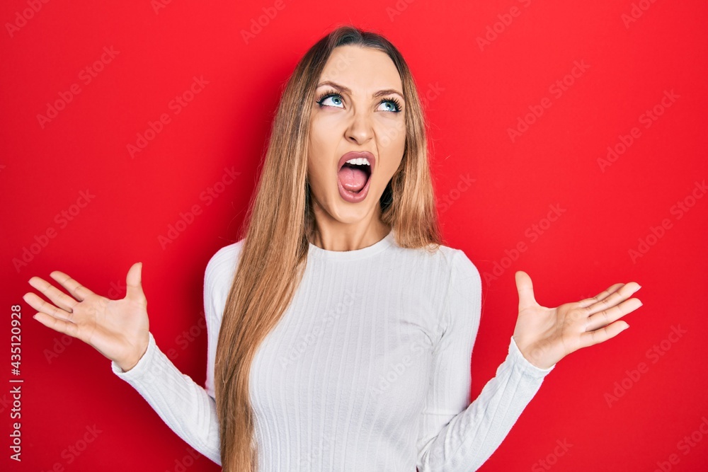 Young blonde girl wearing casual clothes crazy and mad shouting and yelling with aggressive expression and arms raised. frustration concept. Young blonde girl wearing casual clothes crazy and mad shouting and yelling with aggressive expression and arms raised. frustration concept.