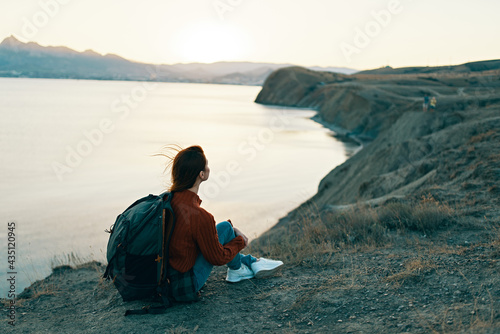 woman hiker sits on the ground in the mountains near the sea at sunset