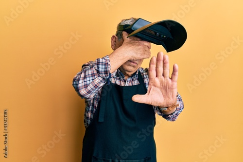Handsome senior man with grey hair wearing welding protection mask covering eyes with hands and doing stop gesture with sad and fear expression. embarrassed and negative concept.