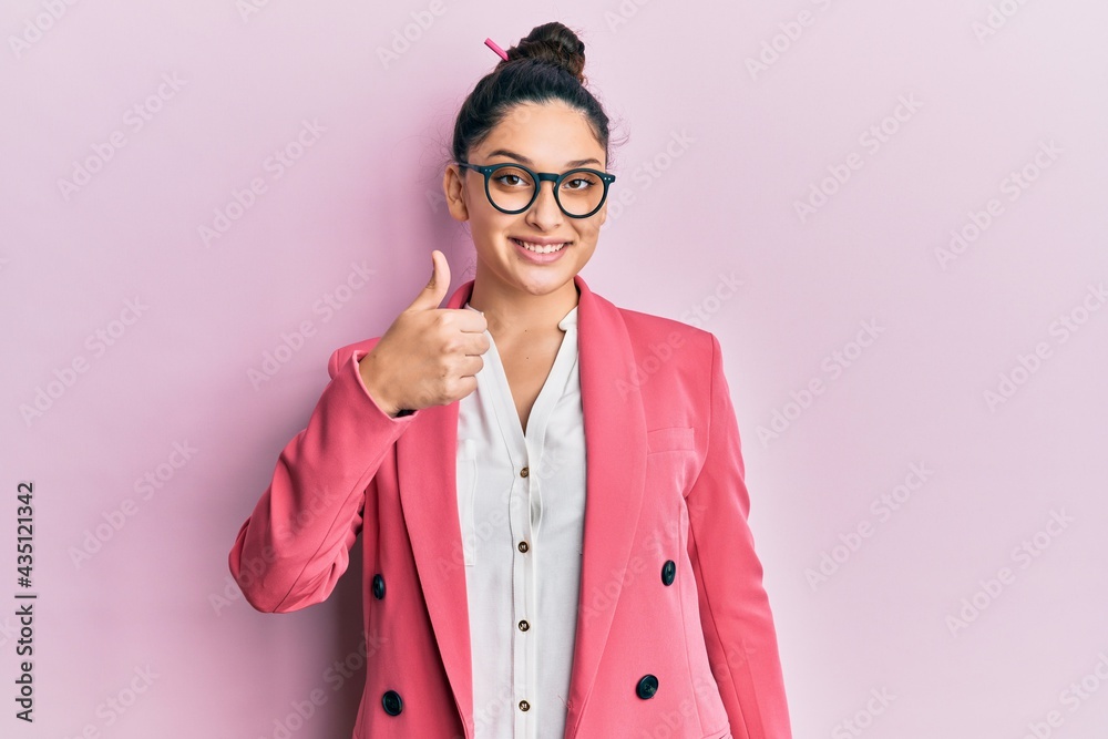 Beautiful middle eastern woman wearing business jacket and glasses doing happy thumbs up gesture with hand. approving expression looking at the camera showing success.