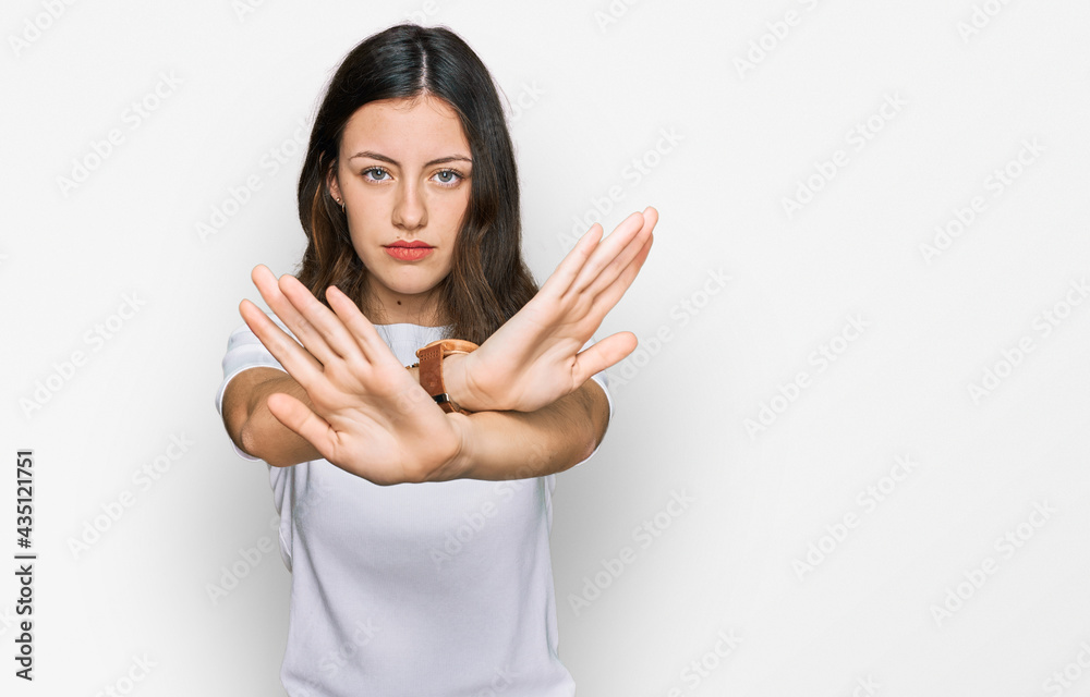 Young beautiful woman wearing casual white t shirt rejection expression crossing arms doing negative sign, angry face Young beautiful woman wearing casual white t shirt rejection expression crossing arms doing negative sign, angry face