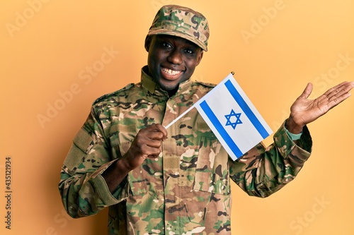 Young african american man wearing army uniform holding israel flag celebrating achievement with happy smile and winner expression with raised hand