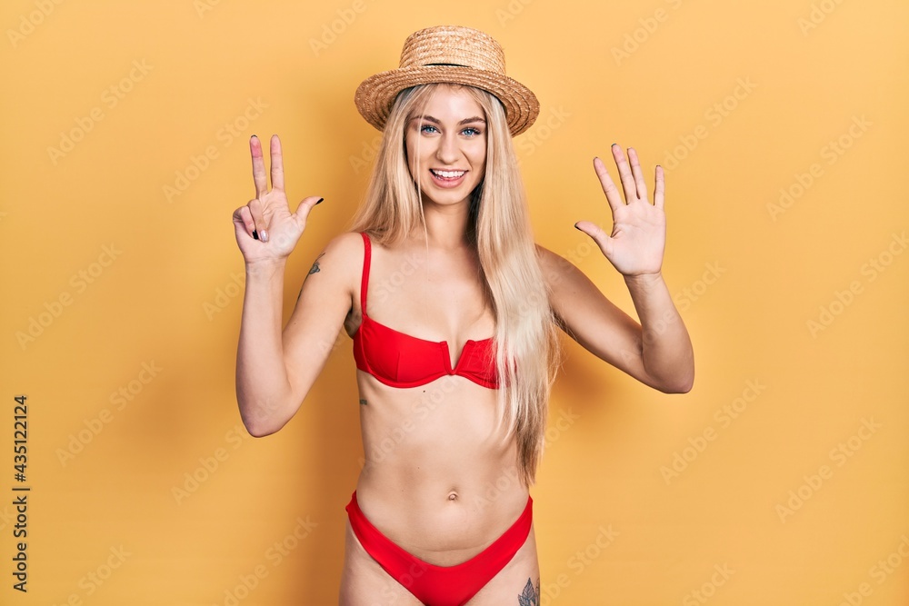 Young caucasian woman wearing bikini and summer hat showing and pointing up with fingers number eight while smiling confident and happy. Young caucasian woman wearing bikini and summer hat showing and pointing up with fingers number eight while smiling confident and happy.