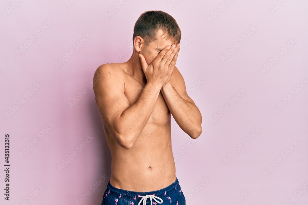 Young caucasian man wearing swimwear with sad expression covering face with hands while crying. depression concept. Young caucasian man wearing swimwear with sad expression covering face with hands while crying. depression concept.