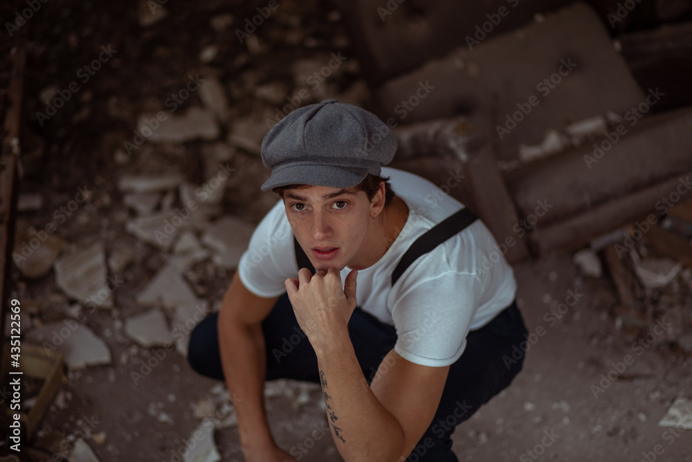 Joven en construcción abandonada vestido con gorro tiradores y camiseta Joven en construcción abandonada vestido con gorro tiradores y camiseta