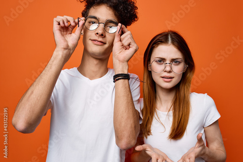 curly guy and a girl in white t-shirts are standing next to each other on an orange background