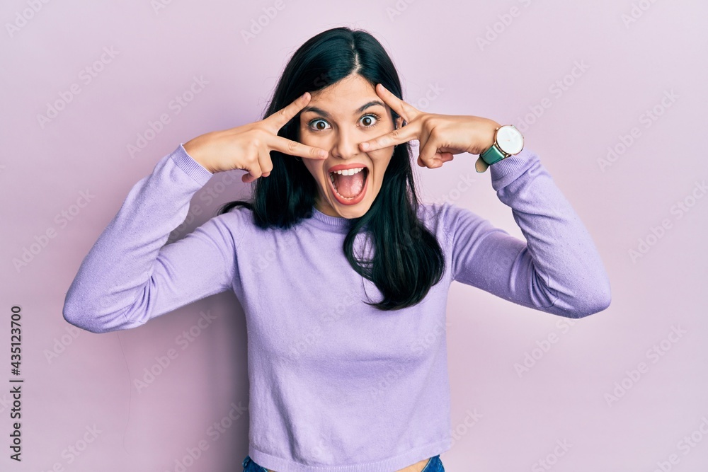 Young hispanic woman wearing casual clothes doing peace symbol with fingers over face, smiling cheerful showing victory Young hispanic woman wearing casual clothes doing peace symbol with fingers over face, smiling cheerful showing victory