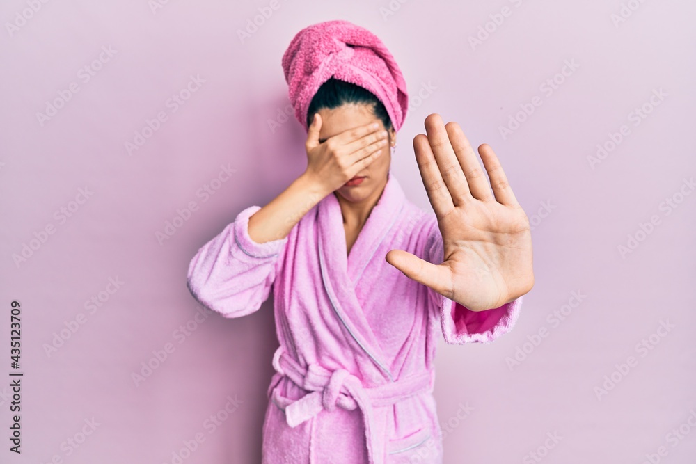 Young hispanic woman wearing shower towel cap and bathrobe covering eyes with hands and doing stop gesture with sad and fear expression. embarrassed and negative concept. Young hispanic woman wearing shower towel cap and bathrobe covering eyes with hands and doing stop gesture with sad and fear expression. embarrassed and negative concept.