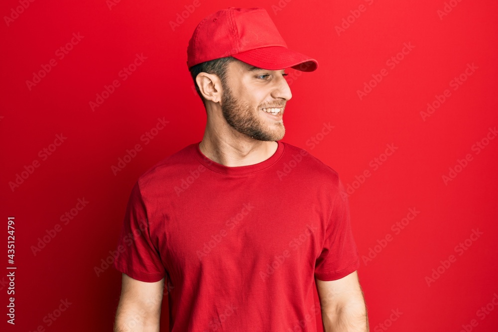 Young caucasian man wearing delivery uniform and cap looking away to side with smile on face, natural expression. laughing confident. Young caucasian man wearing delivery uniform and cap looking away to side with smile on face, natural expression. laughing confident.