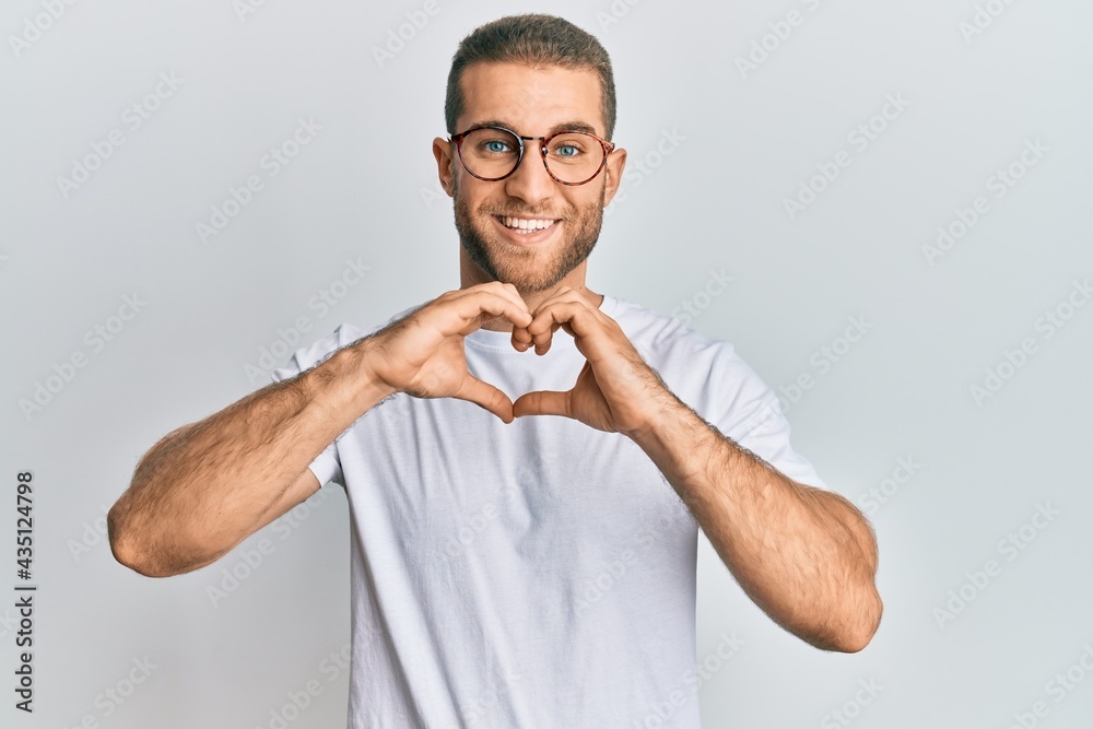 Young caucasian man wearing casual clothes and glasses smiling in love doing heart symbol shape with hands. romantic concept. Young caucasian man wearing casual clothes and glasses smiling in love doing heart symbol shape with hands. romantic concept.