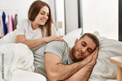 Young caucasian woman looking her sleepy boyfriend at bed.