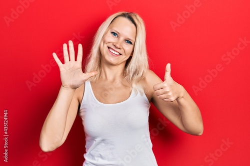 Beautiful caucasian blonde woman wearing casual white t shirt showing and pointing up with fingers number six while smiling confident and happy.