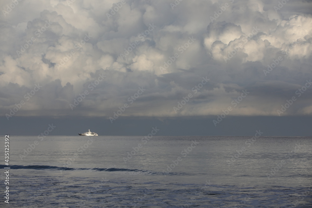 A white ship in the sea on the horizon. An image of an ocean liner on silvery water with lush gray clouds in the morning mist.Photo of a monochrome seascape