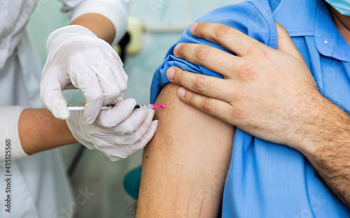 A medical worker gives a syringe injection to a person in the shoulder. Covid vaccination. Vaccination of people. The doctor gives the patient a shot or vaccine in the shoulder. The Covid-19 vaccine.
