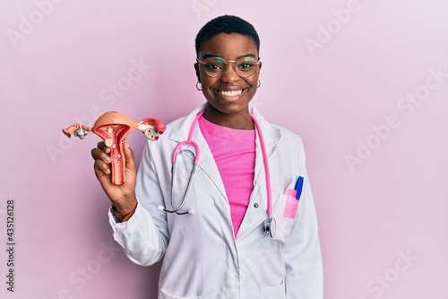 Young african american doctor woman holding anatomical model of female genital organ looking positive and happy standing and smiling with a confident smile showing teeth photo