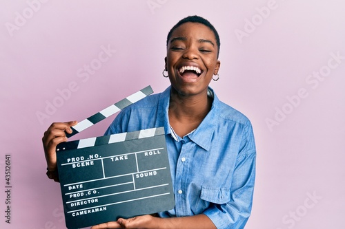 Fototapeta Young african american woman holding video film clapboard smiling and laughing hard out loud because funny crazy joke