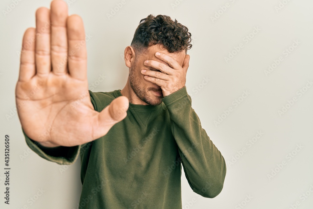 Fototapeta premium Young hispanic man wearing casual clothes covering eyes with hands and doing stop gesture with sad and fear expression. embarrassed and negative concept.