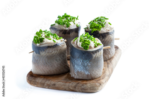 Appetizing pickled herring rolls stuffed with cream cheese and egg mass served on wooden board isolated on white