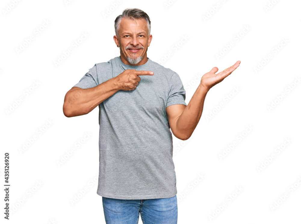 Middle age grey-haired man wearing casual clothes amazed and smiling to the camera while presenting with hand and pointing with finger. Middle age grey-haired man wearing casual clothes amazed and smiling to the camera while presenting with hand and pointing with finger.