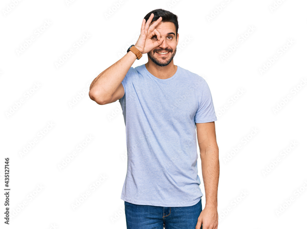 Young hispanic man wearing casual clothes doing ok gesture with hand smiling, eye looking through fingers with happy face.