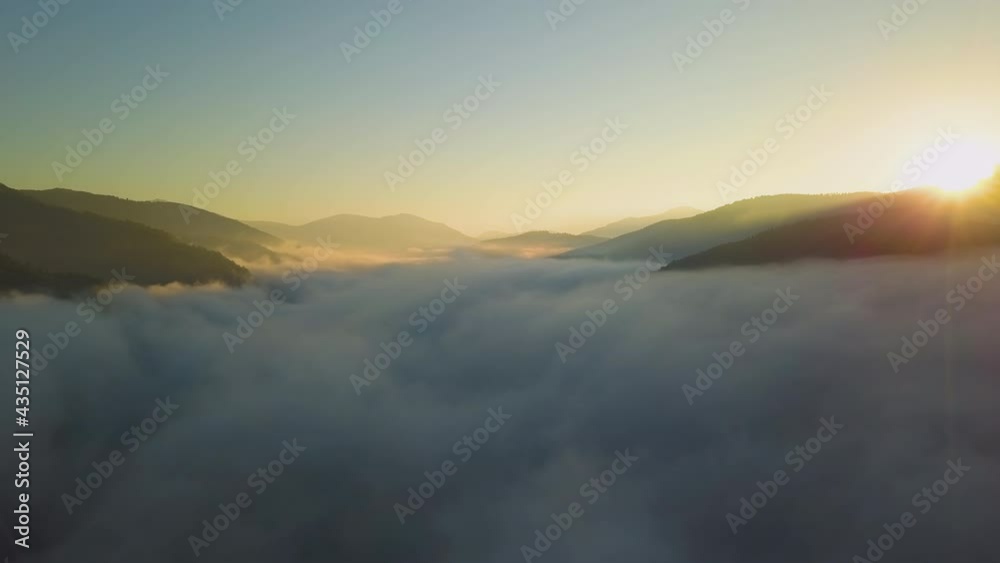 Aerial view of vibrant sunset over white dense foggy clouds with distant dark silhouettes of mountains on horizon. Aerial view of vibrant sunset over white dense foggy clouds with distant dark silhouettes of mountains on horizon.