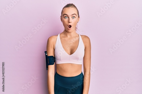 Beautiful blonde woman wearing sportswear and arm band afraid and shocked with surprise expression, fear and excited face. © Krakenimages.com