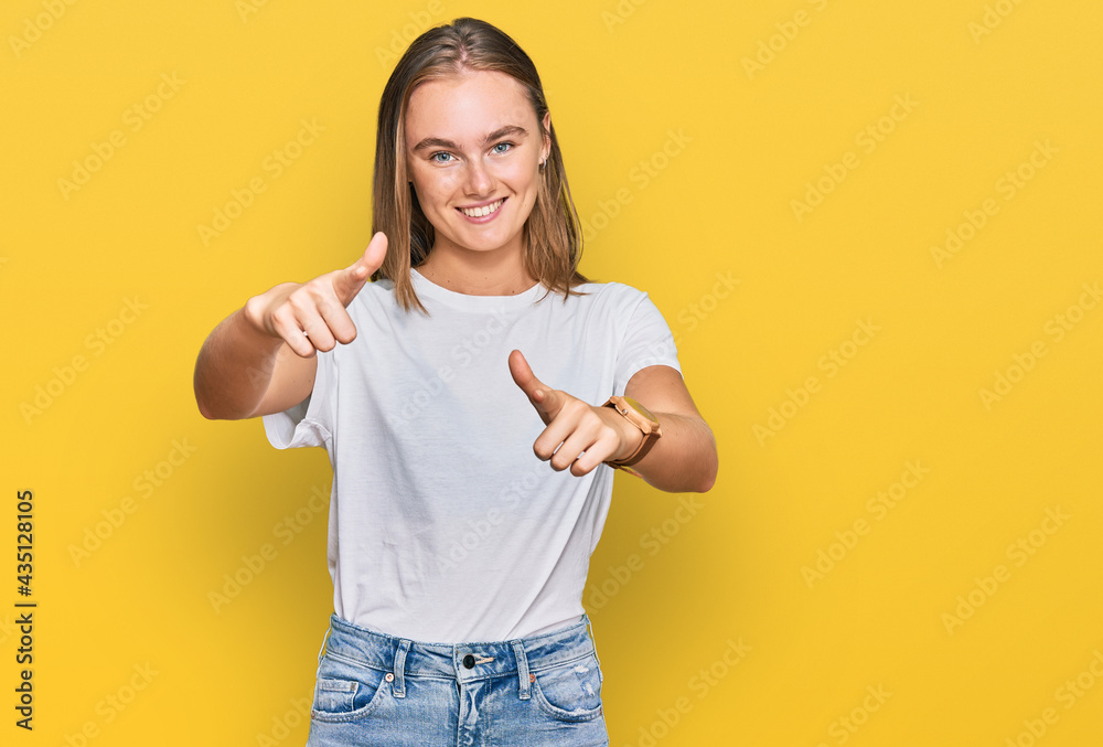 Beautiful young blonde woman wearing casual white t shirt pointing fingers to camera with happy and funny face. good energy and vibes. Beautiful young blonde woman wearing casual white t shirt pointing fingers to camera with happy and funny face. good energy and vibes.