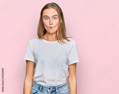 Beautiful young blonde woman wearing casual white t shirt making fish face with lips, crazy and comical gesture. funny expression.