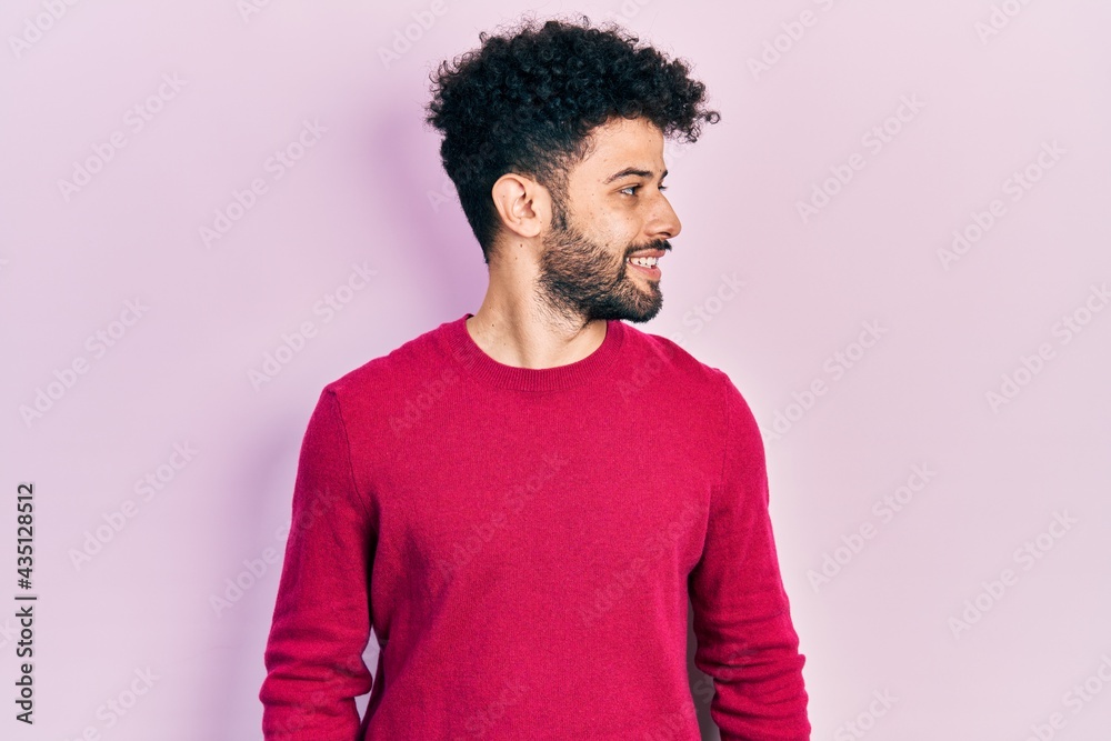 Young arab man with beard wearing casual pink sweater looking away to side with smile on face, natural expression. laughing confident. Young arab man with beard wearing casual pink sweater looking away to side with smile on face, natural expression. laughing confident.