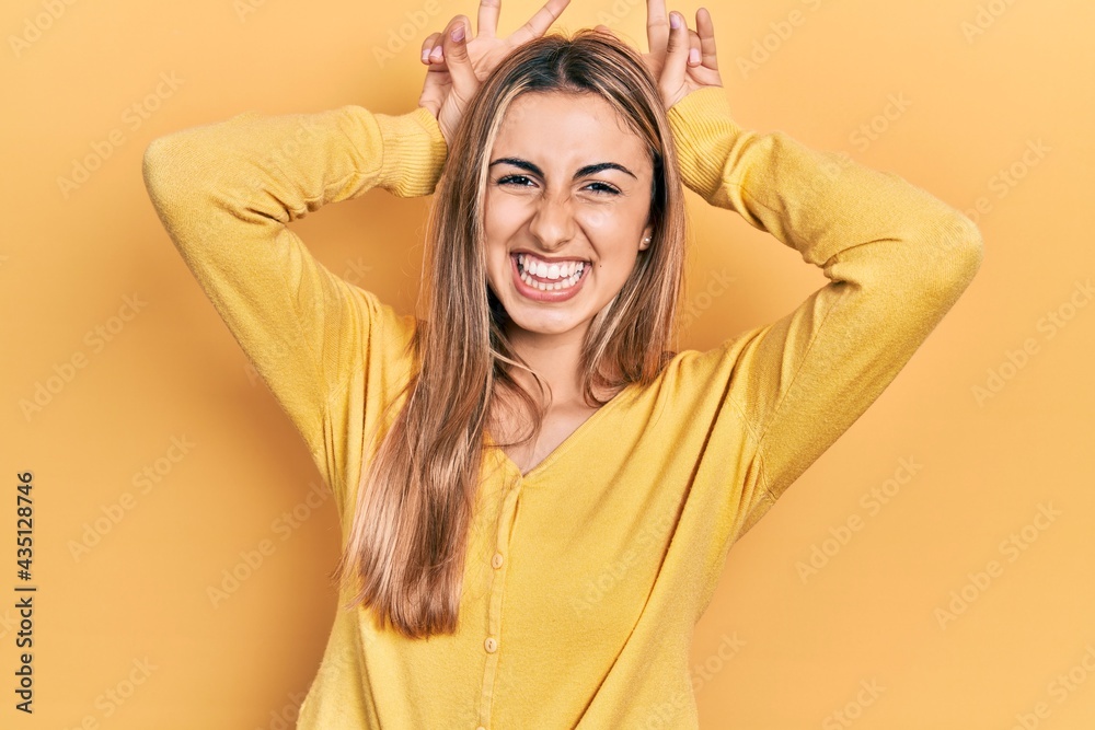 Beautiful hispanic woman wearing casual yellow sweater posing funny and crazy with fingers on head as bunny ears, smiling cheerful Beautiful hispanic woman wearing casual yellow sweater posing funny and crazy with fingers on head as bunny ears, smiling cheerful