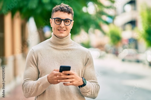 Young hispanic man wearing glasses using smartphone at the city.