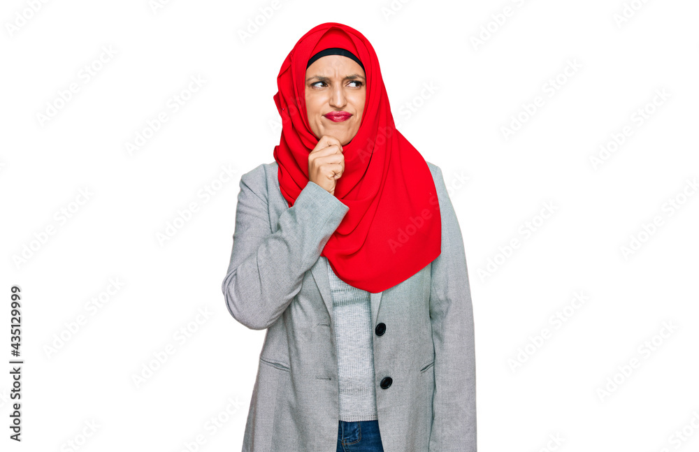 Beautiful hispanic woman wearing traditional islamic hijab scarf serious face thinking about question with hand on chin, thoughtful about confusing idea