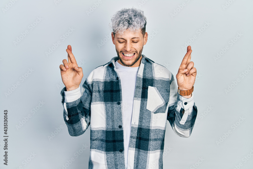 Young hispanic man with modern dyed hair wearing casual shirt gesturing finger crossed smiling with hope and eyes closed. luck and superstitious concept. Young hispanic man with modern dyed hair wearing casual shirt gesturing finger crossed smiling with hope and eyes closed. luck and superstitious concept.
